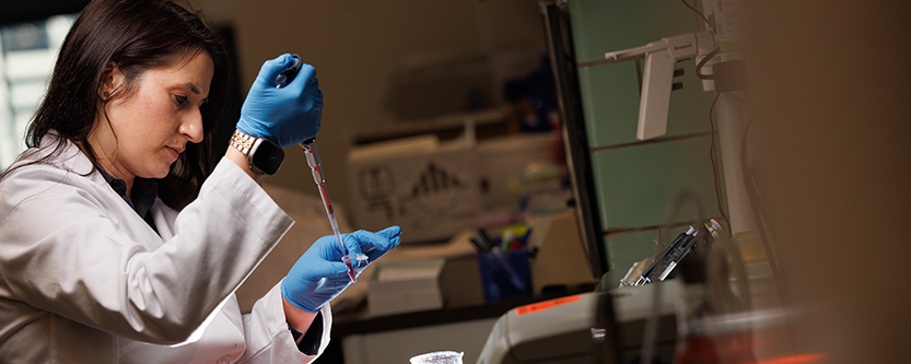 Researcher in lab with glass tube and wearing protective gloves.