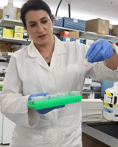 Person in white coat in a lab holding glass vials with fluid in them. 