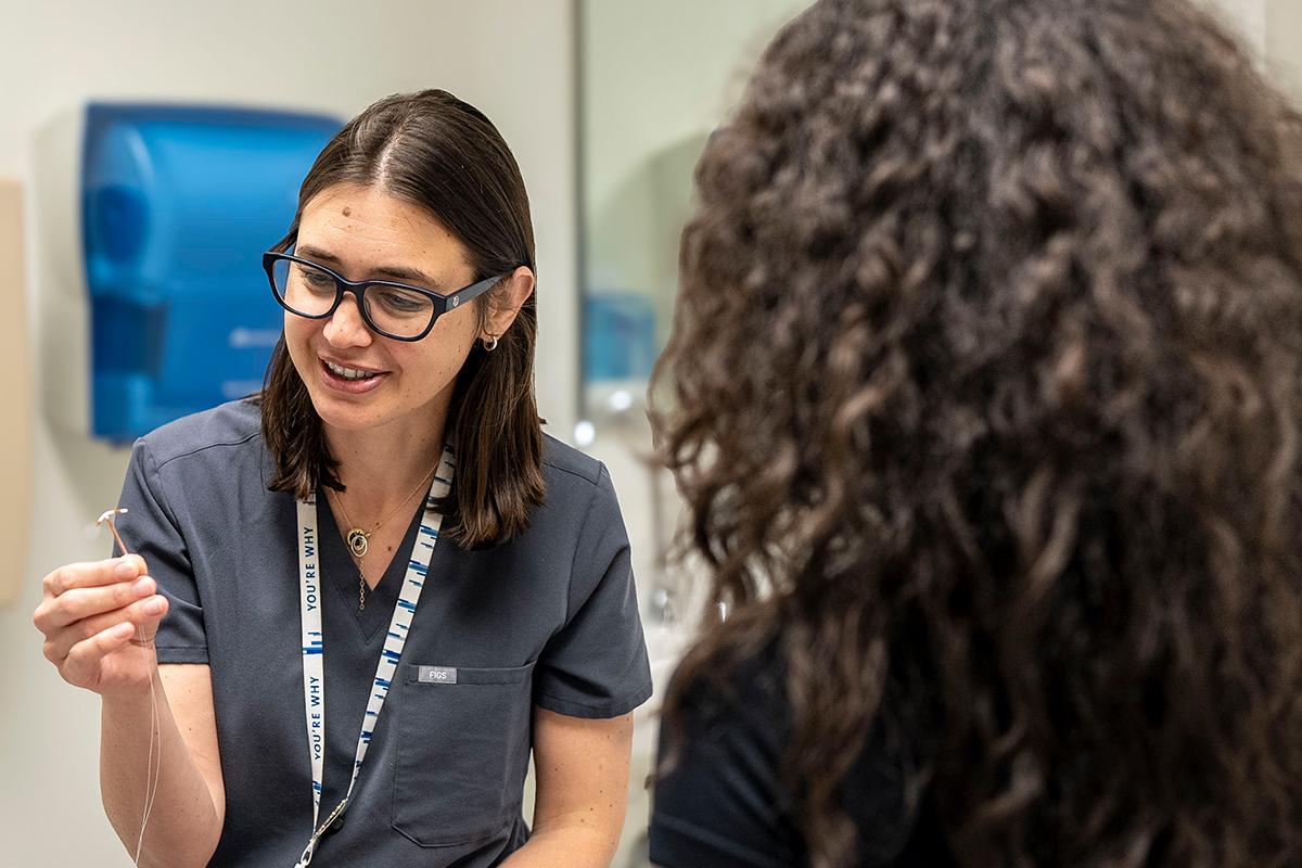 Doctor holding medical device speaking to patient.