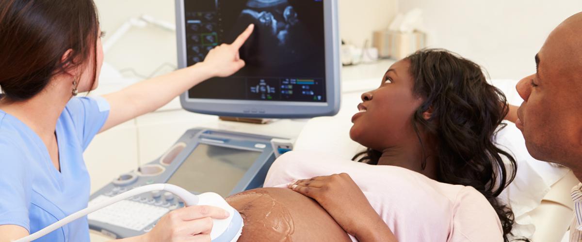 Pregnant patient, sonographer and man looking at ultrasound.