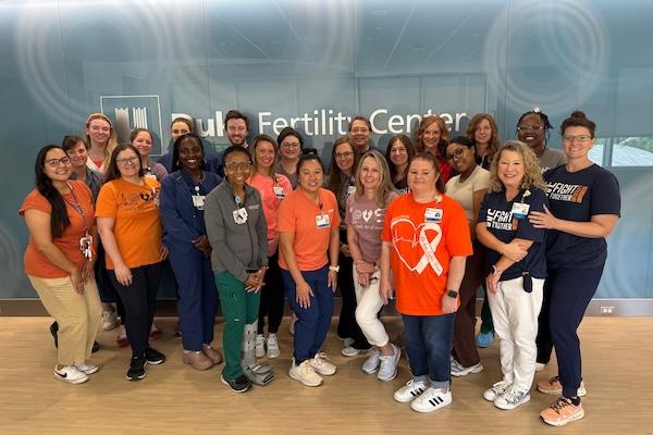 Group of people in front of Duke Fertility Center sign smiling, many wearing orange attire.