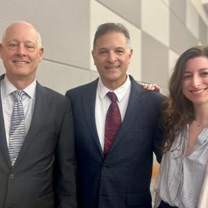 Three people standing and smiling in auditorium.